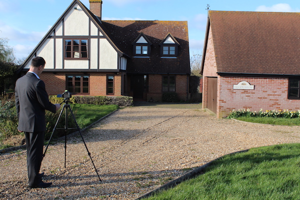 Camera on a tripod with man taking photo of a house