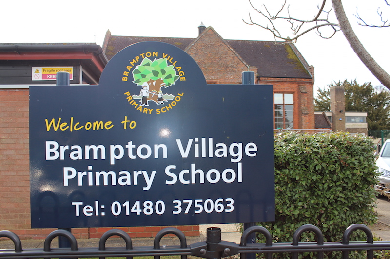 The sign says Welcome to Brampton Village Primary School Tel: 01480 375063. with school behind